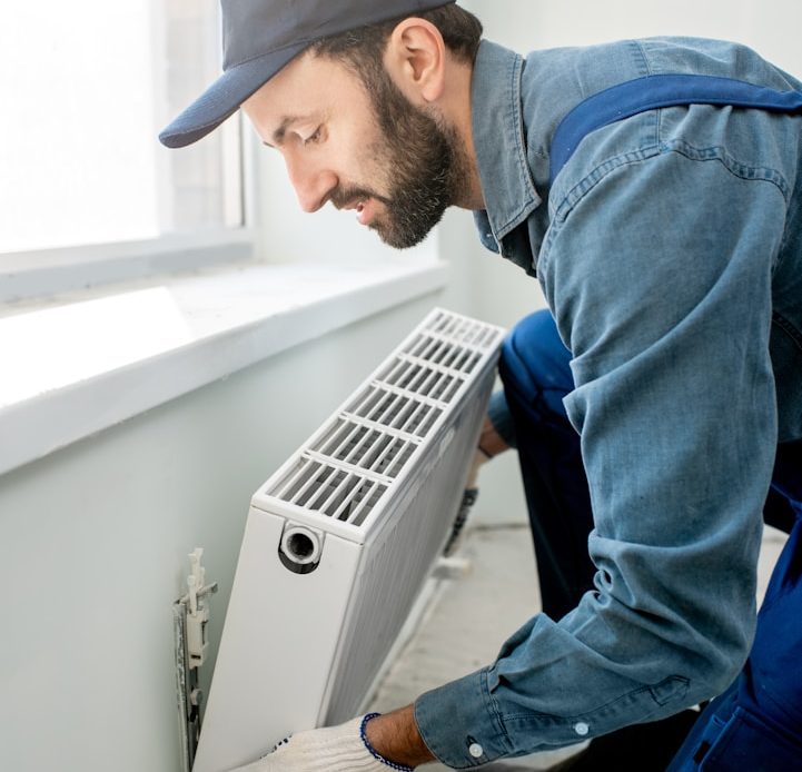 Handwerker installiert eine Heizkörperanlage in einem hellen Raum.